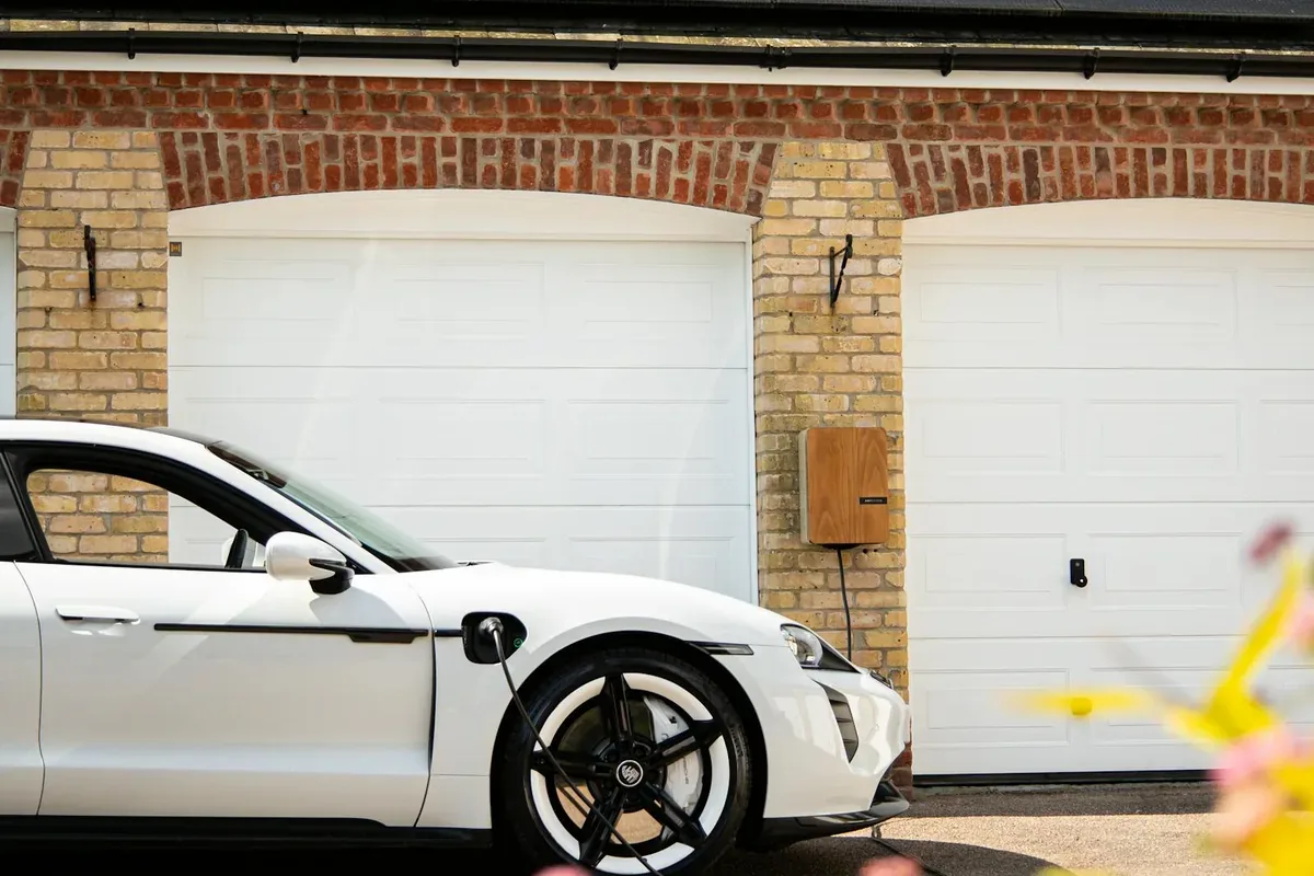 Carport solaire abritant une voiture électrique en recharge sous des panneaux photovoltaïques, devant une maison résidentielle